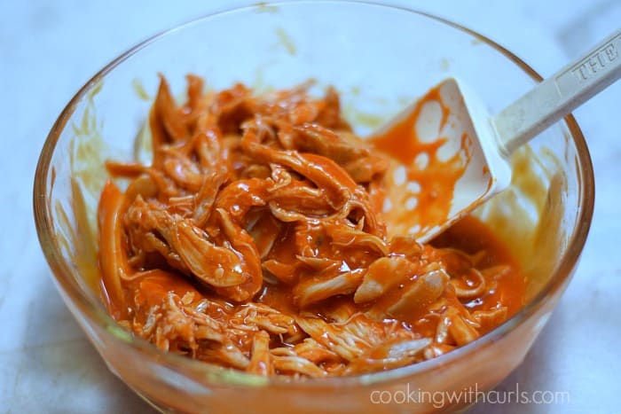 Shredded chicken and hot sauce mixed together in a bowl with a silicone spatula.