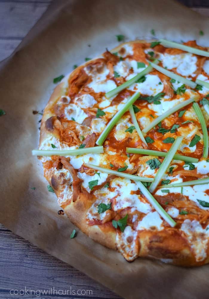 Buffalo Chicken Pizza topped with celery sticks on charred parchment paper. 