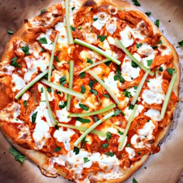 Buffalo Chicken Pizza topped with celery sticks on charred parchment paper.