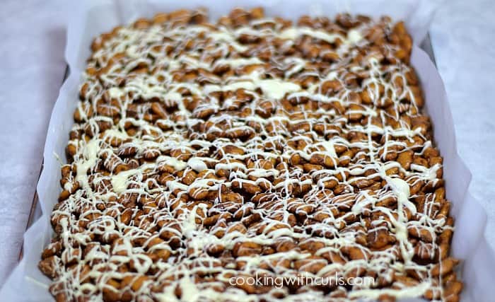 Melted white chocolate drizzled over the cinnamon sugar pretzels on a parchment lined baking sheet.