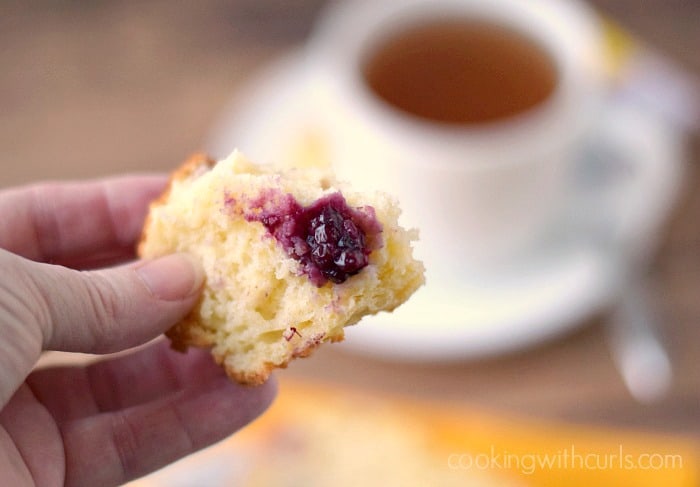 a hand holding a chunk of lemon blackberry bread above a cup of tea