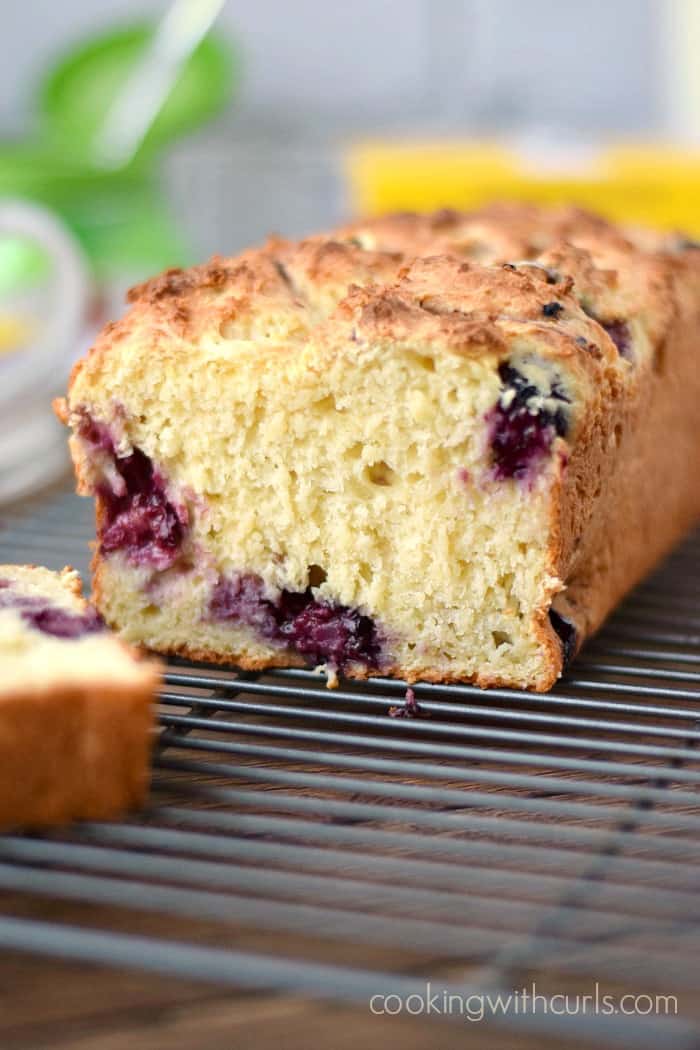 lemon blackberry bread with the end cut off sitting on a wire cooling rack