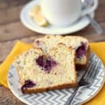 two slices of lemon blackberry bread on a gray and white zigzag patterned plate, sitting on a yellow napkin with a cup of tea in the background