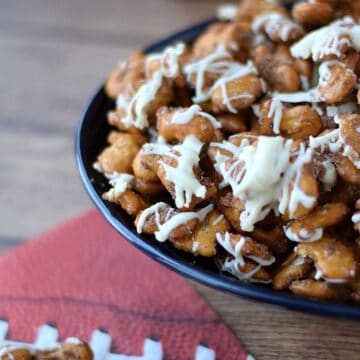 Cinnamon Sugar Goldfish Pretzel Mix drizzled with white chocolate in a dark blue bowl sitting in front of a football napkin.