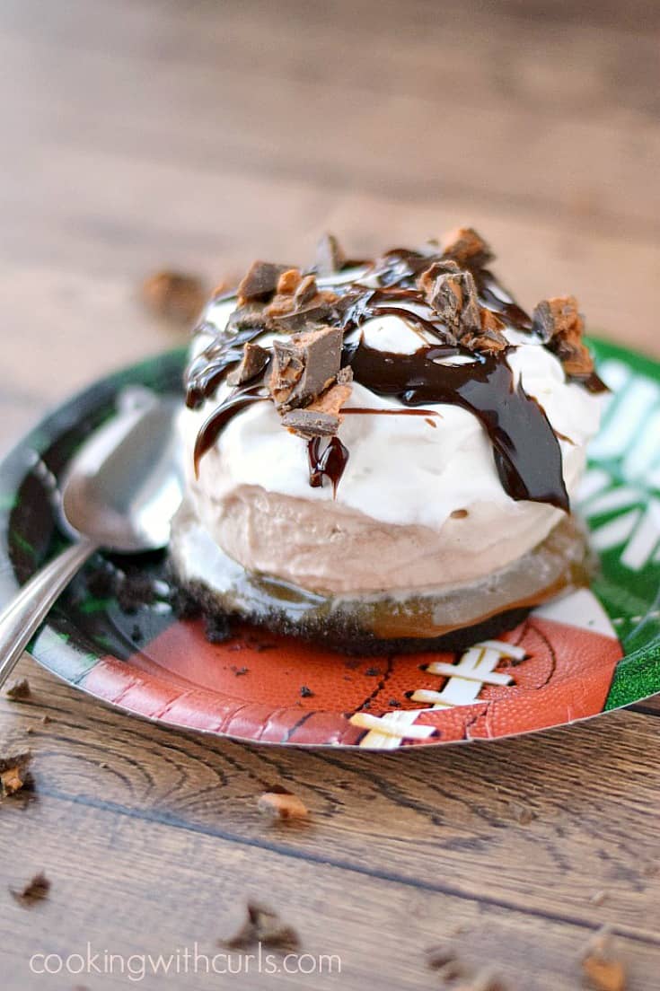An unwrapped ice cream sundae sitting on a football plate with a spoon