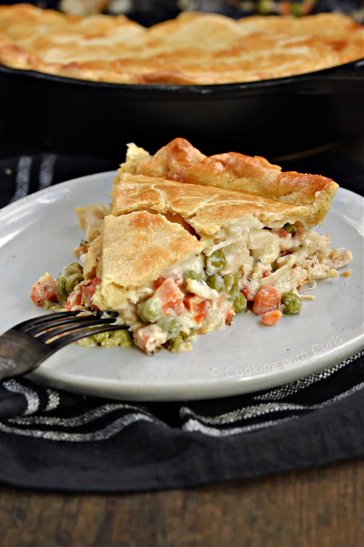 A slice of chicken pot pie with a skillet with the remaining pot pie in the background.
