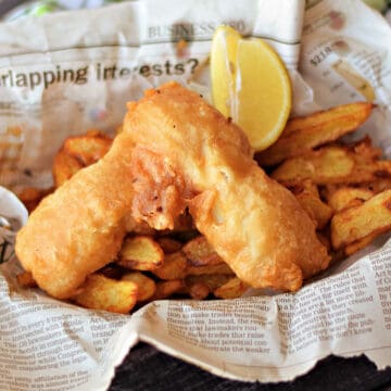 Beer Batter Fish on a bed of French fries in a newspaper lined basket.