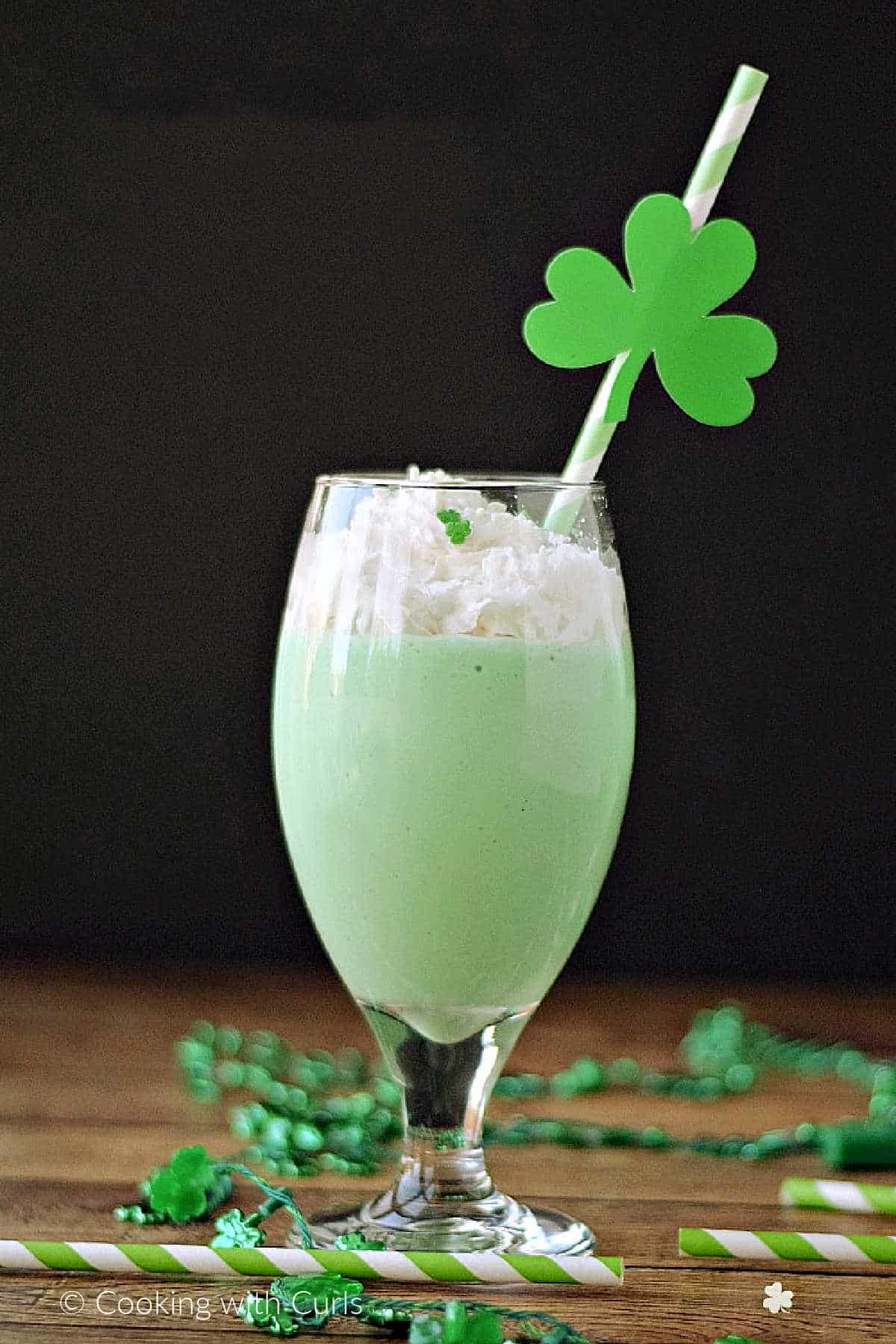 A green shamrock shake in a goblet glass topped with whipped cream and green sprinkles.