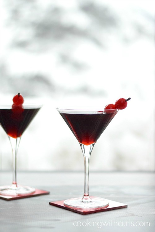 Two Cherry Cheesecake Martinis garnished with skewed cherries in front of a window.