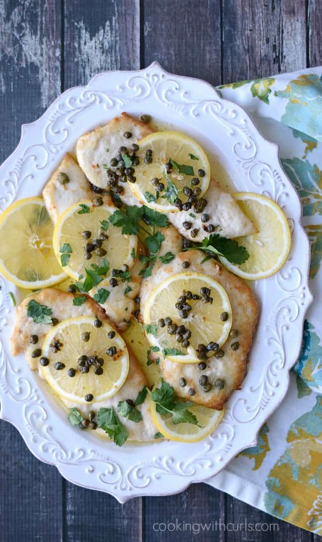 Chicken Scaloppini topped with capers and lemon wheels on a white platter.