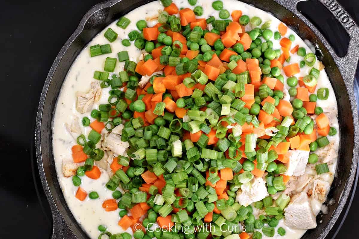 Diced carrots, peas, green onions, chunks of chicken, and creamy gravy in a cast iron skillet. 