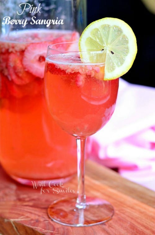 A wine glass filled with pink berry sangria and garnished with a lemon wheel.