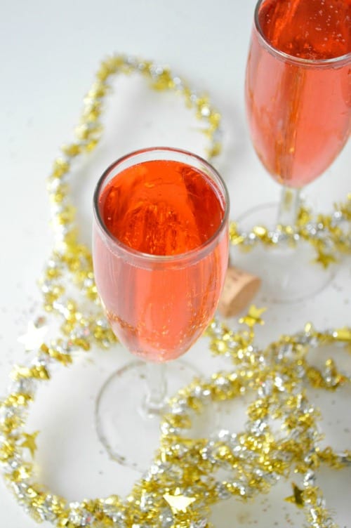 Two Pink Champagne Cocktails in champagne flutes with silver and gold star garland strung around the base.