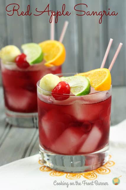 Two Red Apple Sangria cocktails in short glasses garnished with a cherry, lime, orange and melon ball.