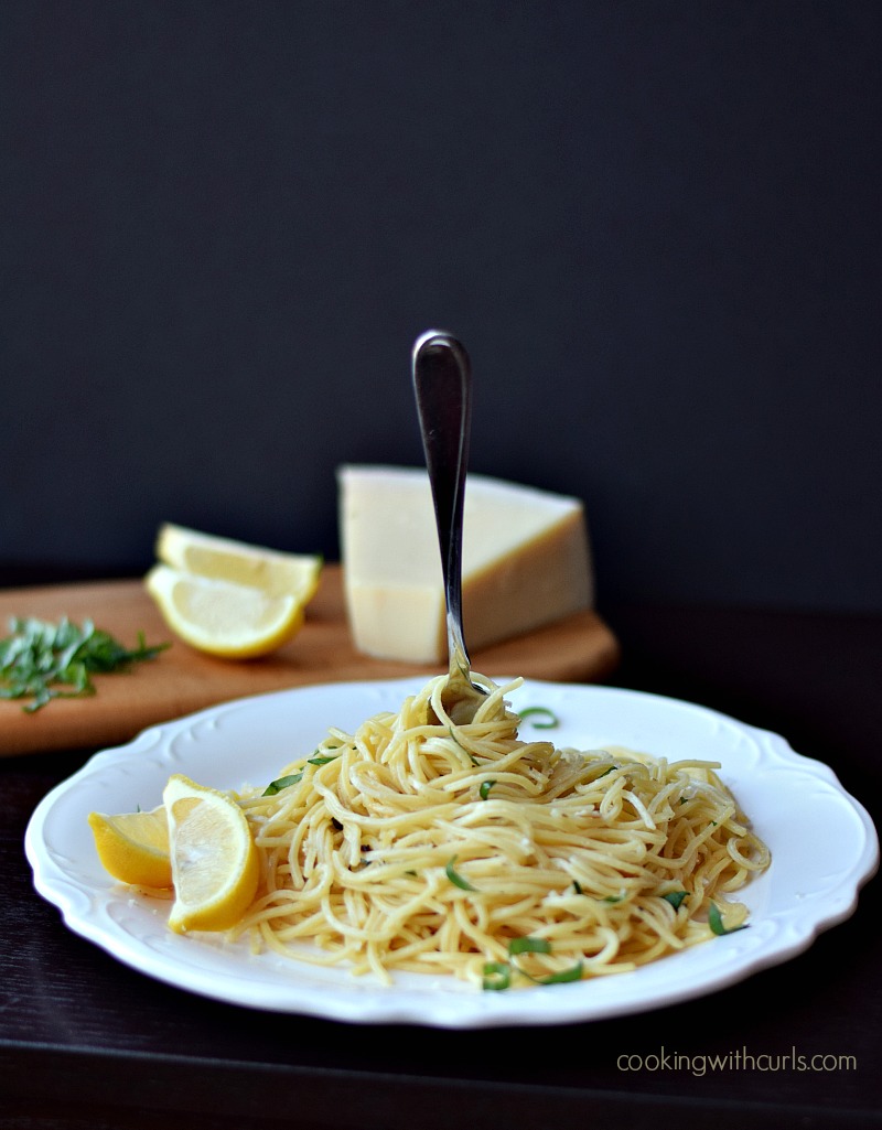 Spaghetti al Limone served on a white plate with lemon wedges and a fork standing up in the center.