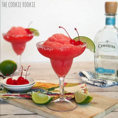 Two frozen cherry limeade margaritas garnished with cherries and lime wedges.