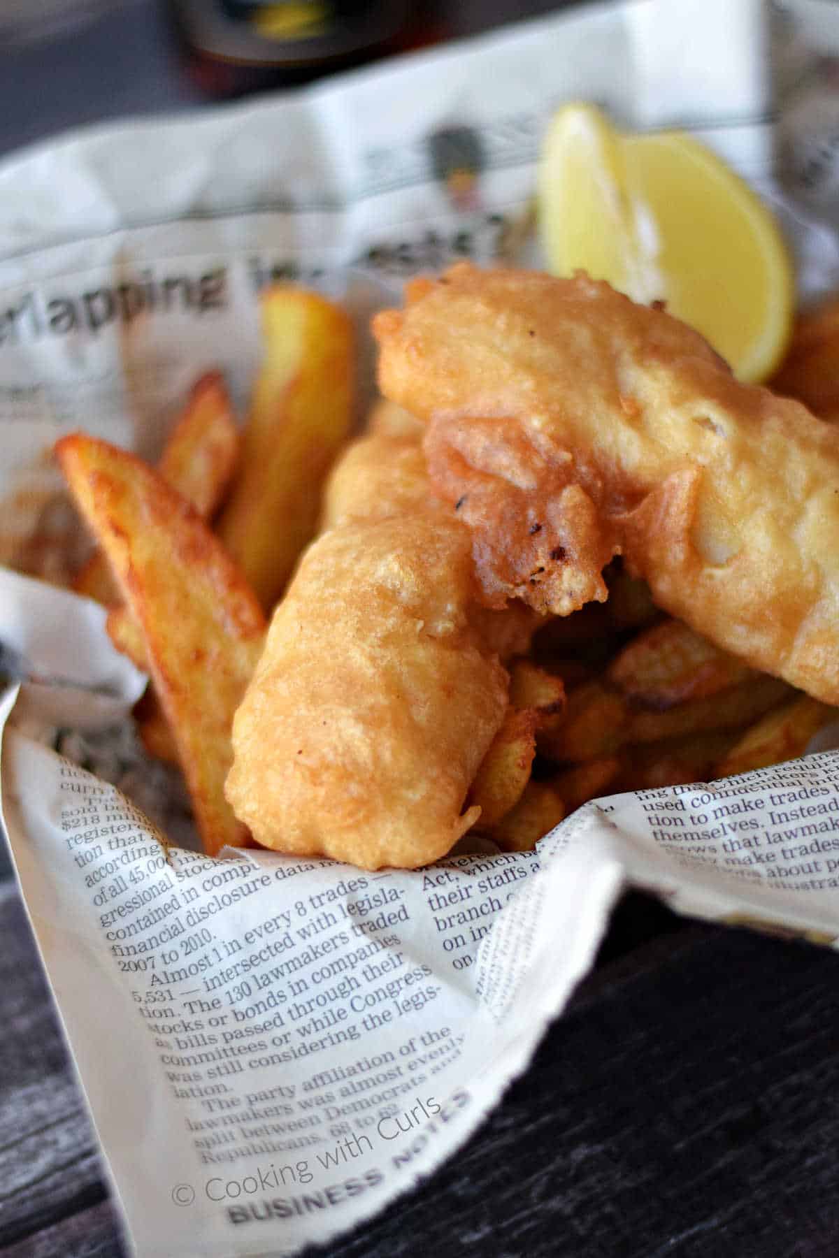 Two pieces of Beer Batter Fish on a pile of chips in a newspaper lined basket.
