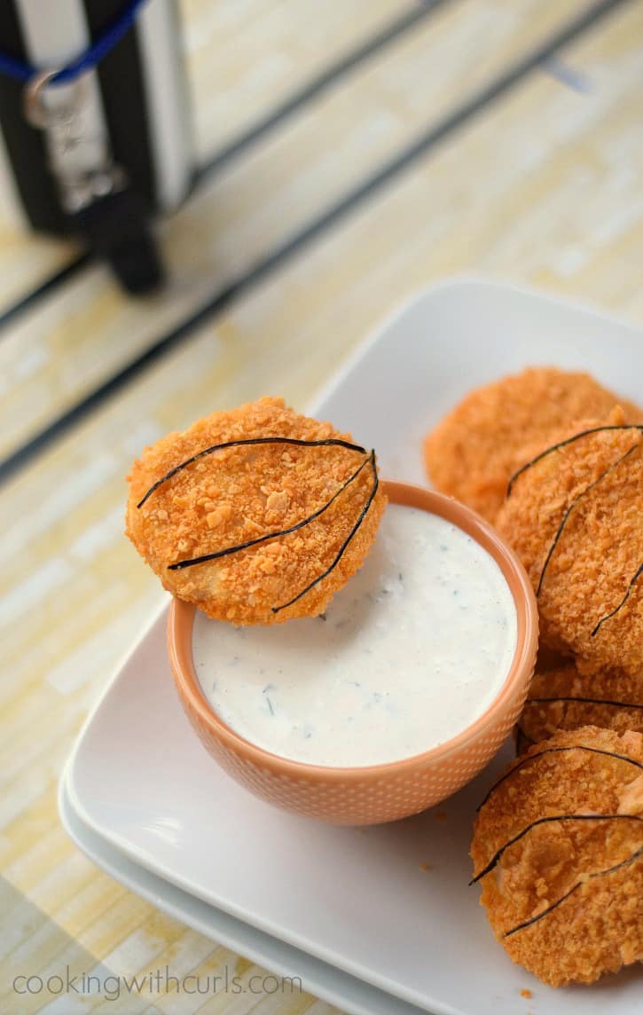 cheeze-it covered chicken tenders surrounding a small bowl of ranch dressing sitting on a basketball court table cloth
