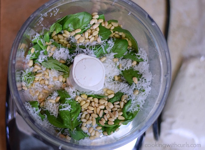 Fresh basil leaves, pine nuts and grated parmesan cheese in a food processor bowl.