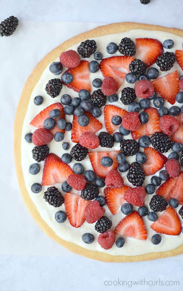 Looking down on a fresh blackberries, blueberries, strawberries and raspberries on top of a cream cheese topped giant sugar cookie.