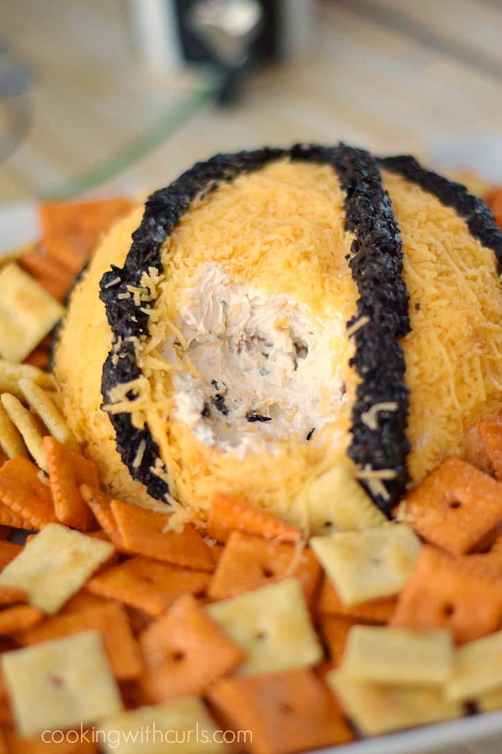 a cheddar cheese covered cheeseball with a large scoop out of the side surrounded by crackers