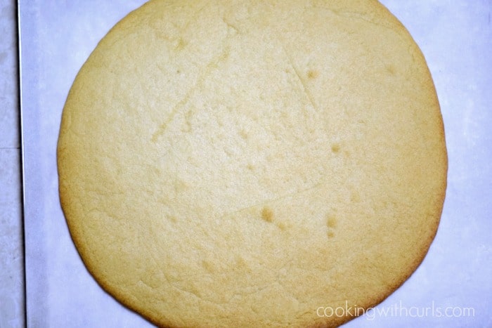 A baked, giant sugar cookie on a parchment lined baking sheet.