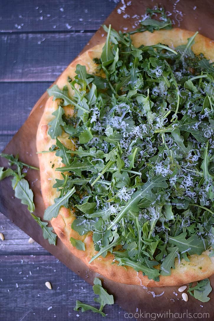 Pizza topped with pesto, arugula, and grated parmesan cheese.