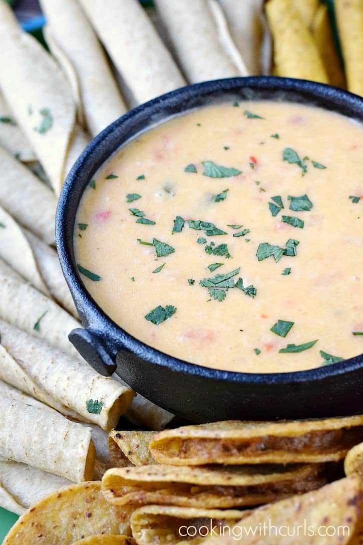 queso blanco dip in a black bowl surrounded by taquitos and mini tacos