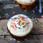 Homemade Funfetti Cupcakes on a wooden background with sprinkles everywhere