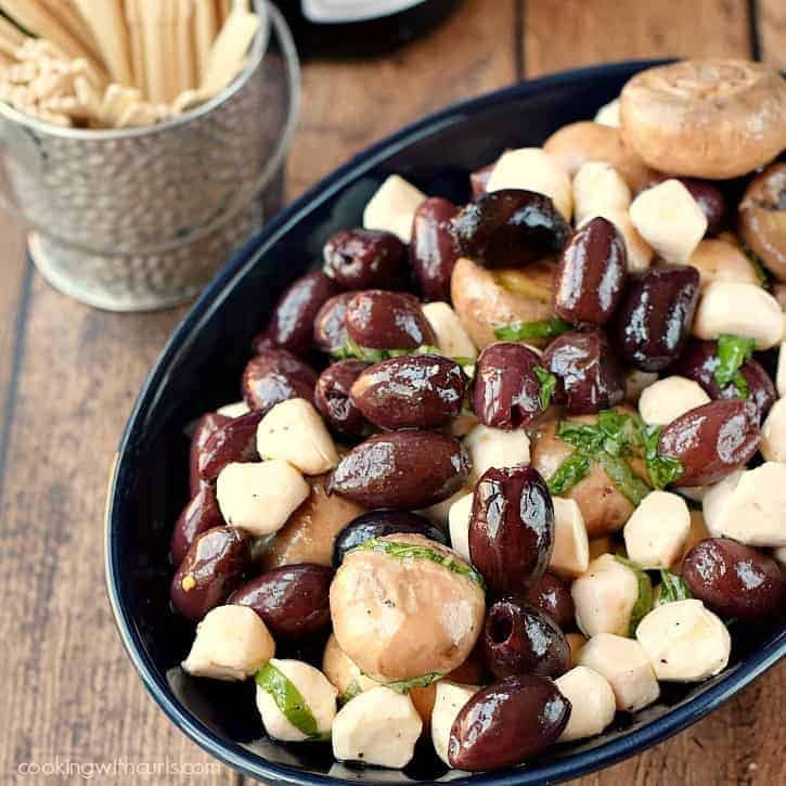 Marinated Olives, Mushrooms, and Mozzarella in an oval, dark blue bowl with toothpicks in a small metal pail