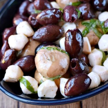 marinated mushrooms, olives, and mozzarella pearls in a dark blue oval bowl