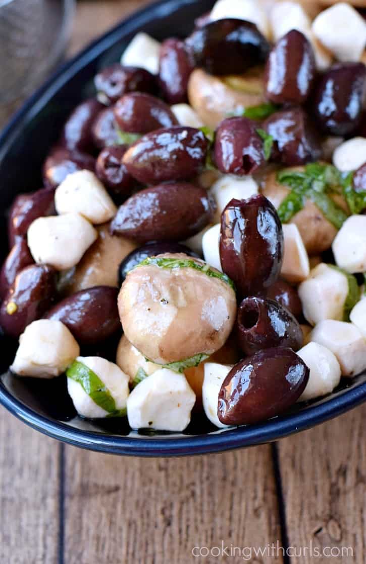 marinated mushrooms, olives, and mozzarella pearls in a dark blue oval bowl