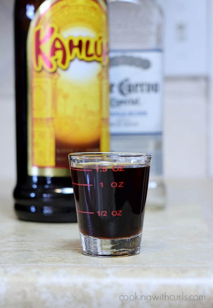 A shot glass with 1.5 ounces of Kahlua with the bottle in the background.
