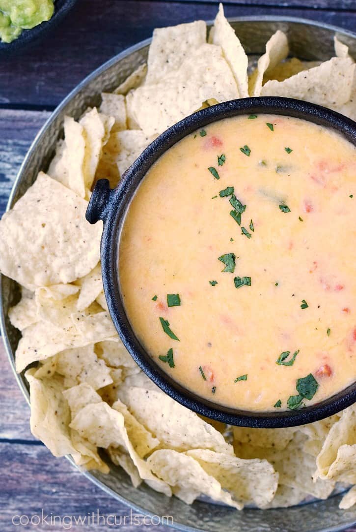 queso blanco dip in a black bowl surrounded by tortilla chips in a round metal serving platter