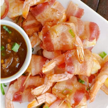Looking down on a stack of bacon wrapped shrimp and pineapple on a plate with a bowl of teriyaki sauce.