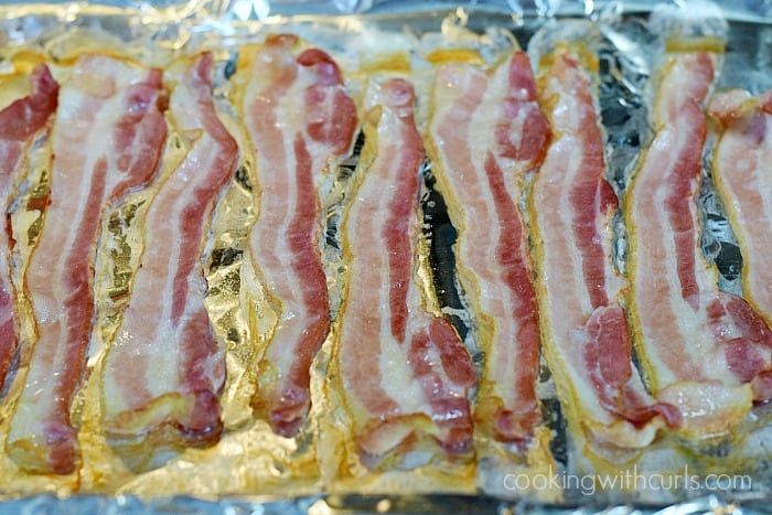 Partially cooked strips of bacon on a foil lined baking sheet.