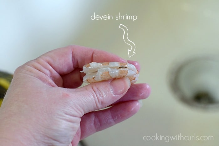 A hold holding a raw shrimp with the backside cut showing the vein.