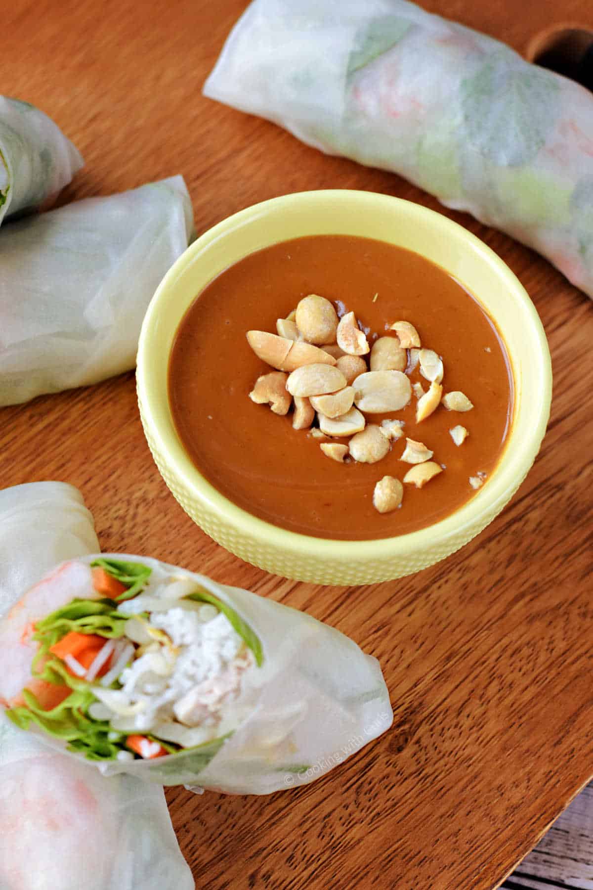 A small bowl filled with Vietnamese peanut sauce with chopped peanuts sprinkled on top and surrounded by fresh spring rolls.