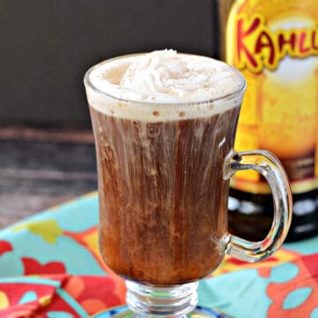 Coffee cocktail in a tall glass mug topped with whipped cream, with a bottle of Kahlua in the background.