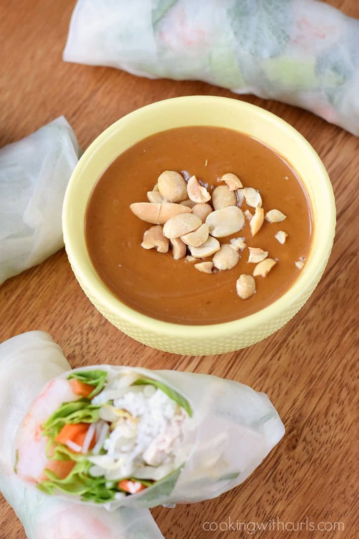 A small yellow bowl filled with peanut top with chopped peanuts sprinkled on top and surrounded by spring rolls.