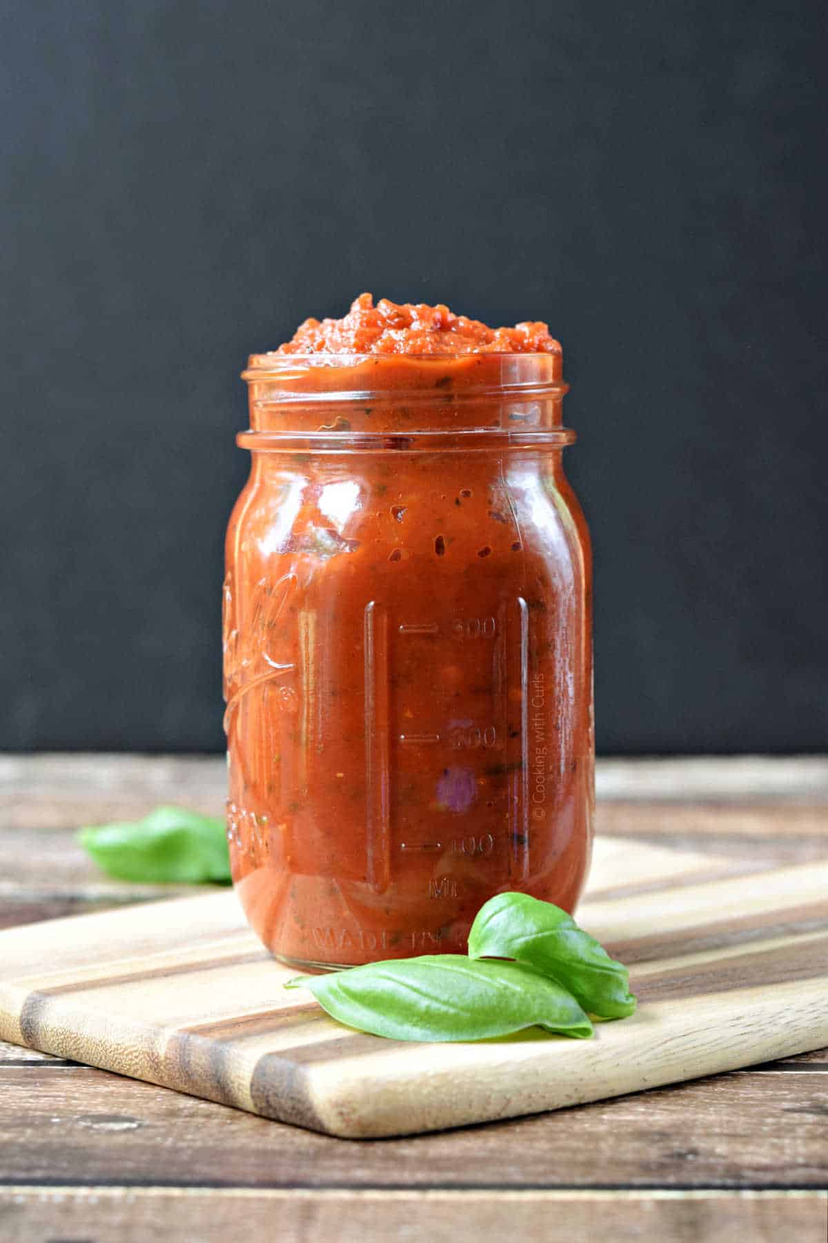 Classic Marinara Sauce in a mason jar with fresh basil leaves on the side.