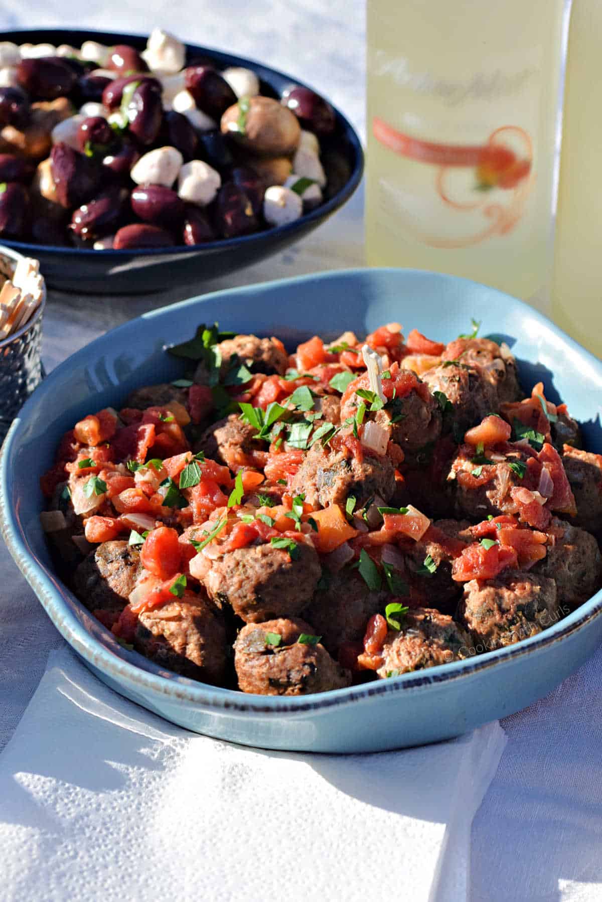 Spanish meatballs with tomato sauce in a serving bowl with a bowl of olives and mushrooms in the background.