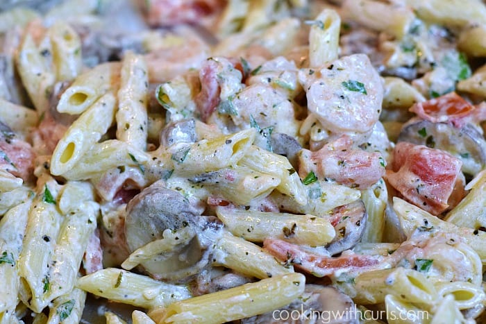 Creamy sauce mixed with shrimp, sliced mushrooms, and chopped tomatoes thinned with hot pasta water in a skillet.