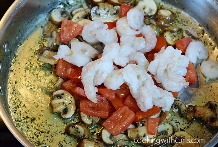 Raw shrimp, chopped tomatoes piled on top of the mushrooms in a large skillet.