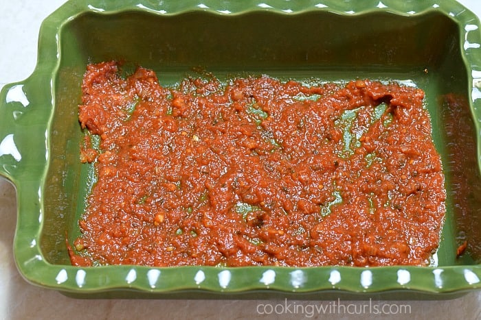 Tomato sauce spread on the bottom of a baking dish.