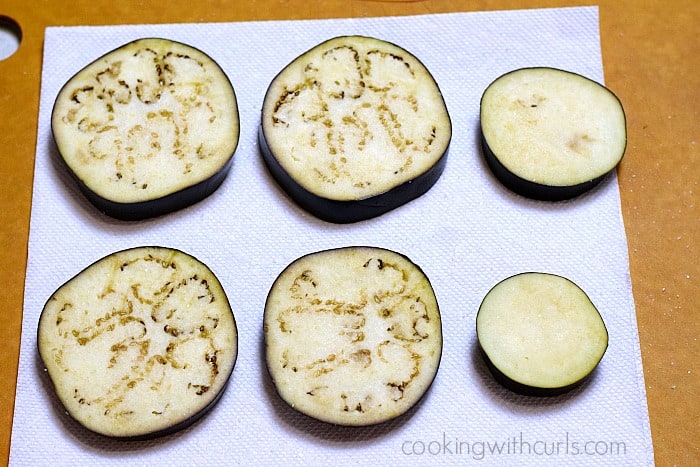 Six slices of eggplant on a paper towel.