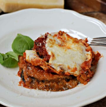 Eggplant parmesan on a plate with a wedge of parmesan cheese in the background.