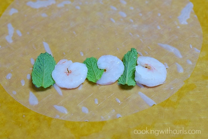 Three shrimp and three mint leaves laying on the wrapper.