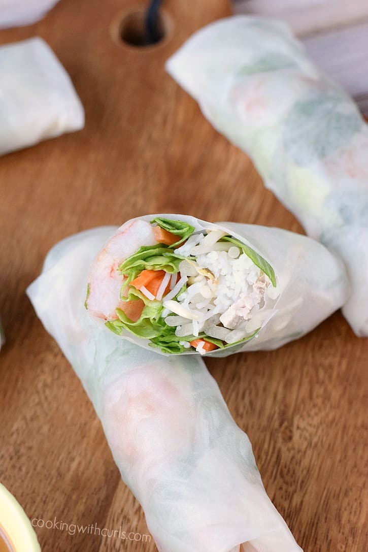 spring rolls laying on a wooden board with a cut roll resting on top
