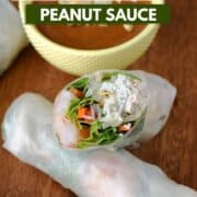 Spring rolls laying on a wooden board with a diagonal cut half laying on top and a yellow bowl of peanut sauce in the left corner and title graphic across the top.